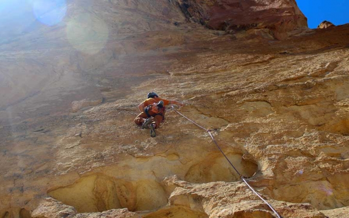 Wearing safety gear and secured by ropes, a person climbs a steep rock wall.